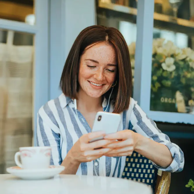 Eine Frau sitzt im Kaffee und chattet via WhatsApp